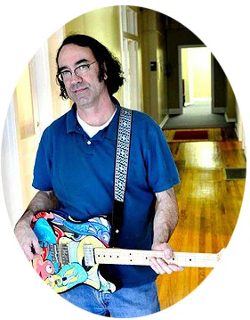 Forrest York holding a hand-painted electric guitar in the shop hallway
